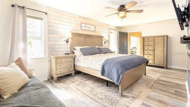 bedroom featuring ceiling fan, wooden walls, and light hardwood / wood-style flooring