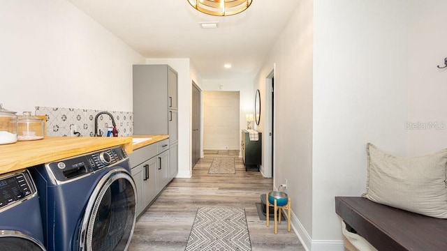 clothes washing area with washing machine and dryer, sink, cabinets, and light wood-type flooring