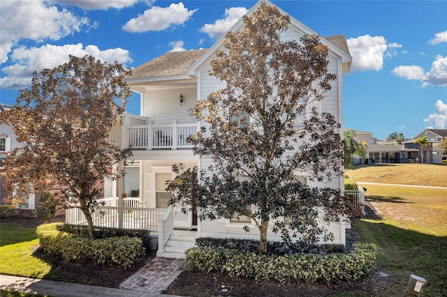 view of property hidden behind natural elements featuring a porch, a balcony, and a front lawn