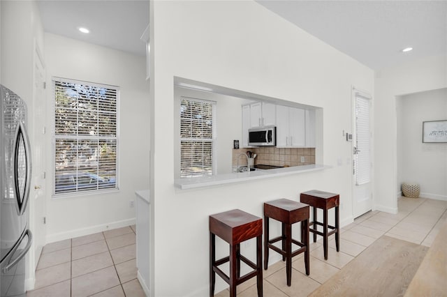 kitchen featuring tasteful backsplash, white cabinetry, light tile patterned floors, and appliances with stainless steel finishes