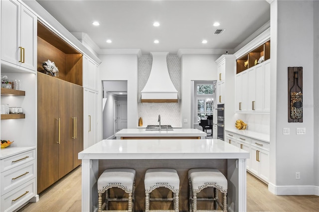 kitchen with appliances with stainless steel finishes, white cabinets, backsplash, a kitchen breakfast bar, and a kitchen island with sink