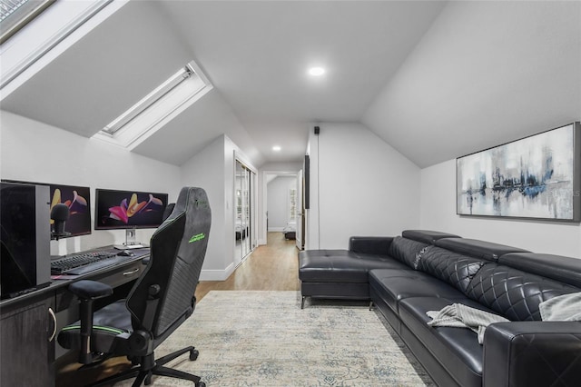 office area with vaulted ceiling with skylight and light hardwood / wood-style floors