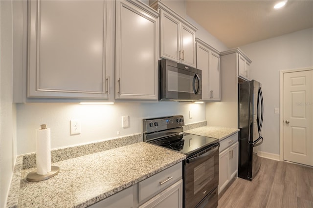 kitchen featuring light stone counters, light hardwood / wood-style flooring, and black appliances