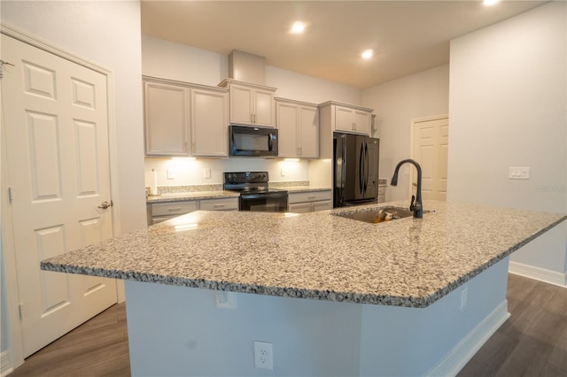 kitchen with dark hardwood / wood-style flooring, light stone counters, sink, black appliances, and a breakfast bar area