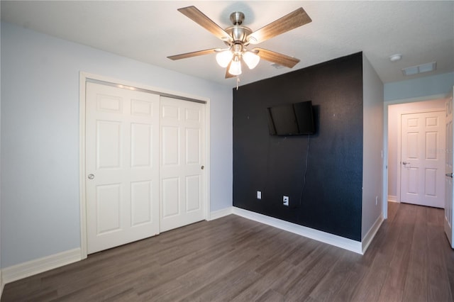 unfurnished bedroom with a textured ceiling, ceiling fan, dark wood-type flooring, and a closet