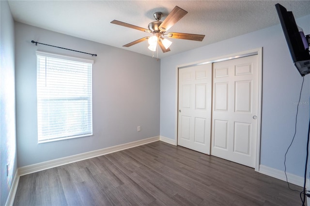 unfurnished bedroom featuring dark hardwood / wood-style flooring, a closet, multiple windows, and ceiling fan