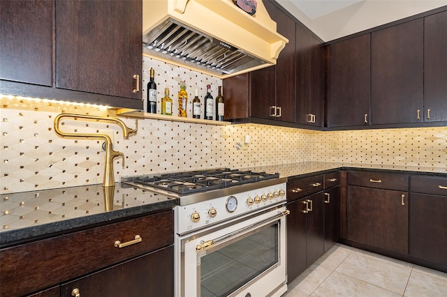 kitchen with premium range hood, dark stone countertops, light tile patterned floors, stainless steel range, and dark brown cabinetry