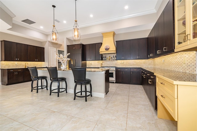 kitchen with custom exhaust hood, a breakfast bar, an island with sink, tasteful backsplash, and premium appliances