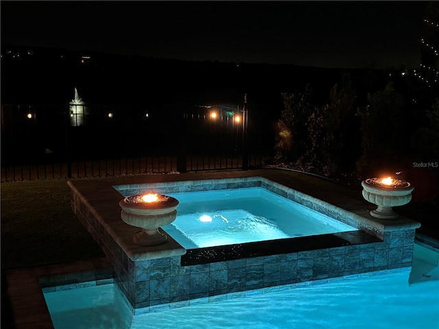 pool at night featuring an in ground hot tub