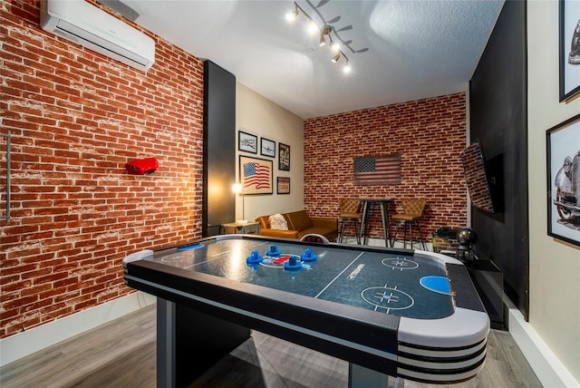 recreation room with brick wall, an AC wall unit, hardwood / wood-style floors, track lighting, and a textured ceiling