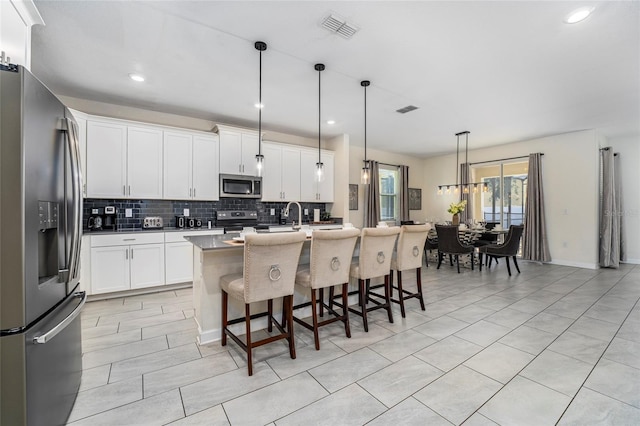 kitchen with white cabinetry, hanging light fixtures, stainless steel appliances, an island with sink, and a breakfast bar