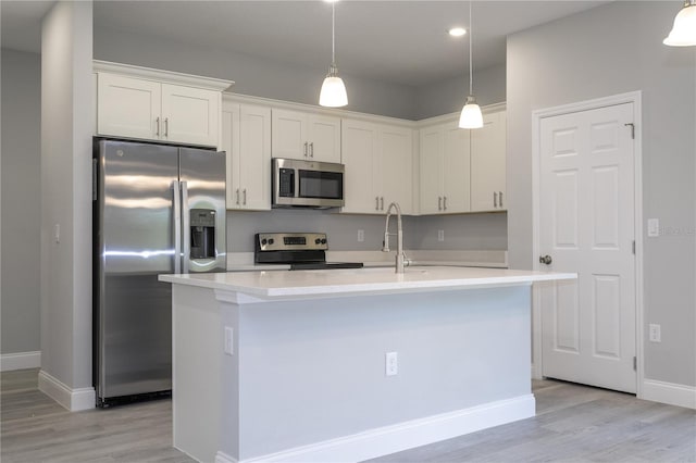 kitchen featuring appliances with stainless steel finishes, decorative light fixtures, light hardwood / wood-style flooring, white cabinets, and an island with sink