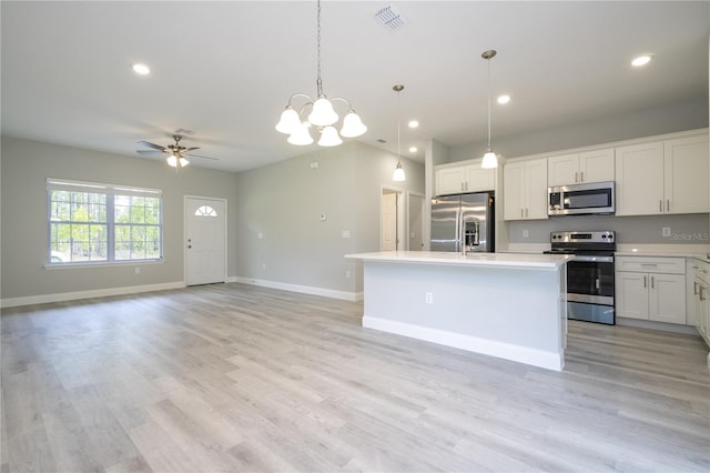 kitchen with appliances with stainless steel finishes, ceiling fan with notable chandelier, pendant lighting, white cabinets, and an island with sink