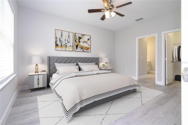 bedroom featuring connected bathroom, ceiling fan, a walk in closet, a closet, and light wood-type flooring