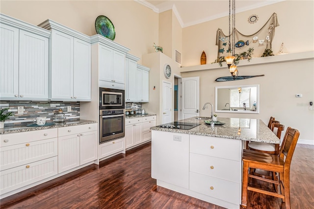 kitchen with stainless steel appliances, light stone counters, a kitchen breakfast bar, an island with sink, and backsplash