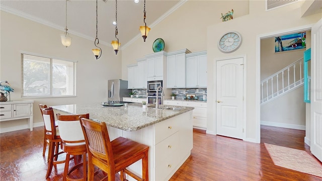 kitchen with high vaulted ceiling, white cabinetry, an island with sink, a kitchen bar, and hanging light fixtures