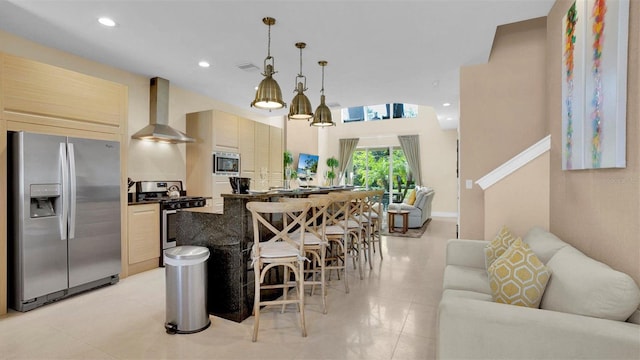 kitchen with wall chimney range hood, pendant lighting, a breakfast bar, a kitchen island, and appliances with stainless steel finishes