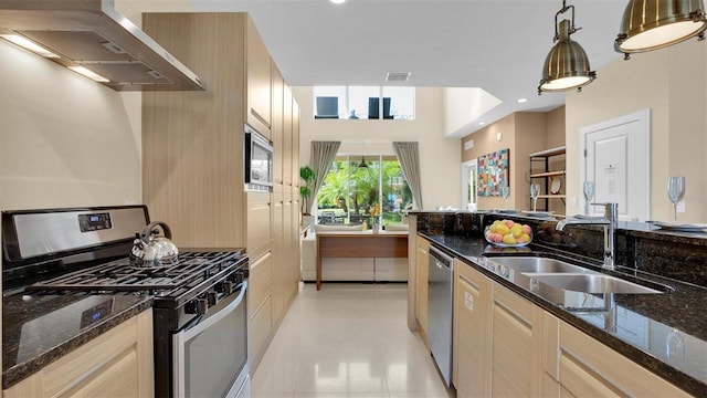 kitchen featuring light brown cabinetry, stainless steel appliances, sink, wall chimney range hood, and pendant lighting