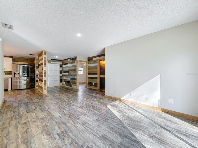 unfurnished living room featuring hardwood / wood-style flooring, wood walls, and a textured ceiling