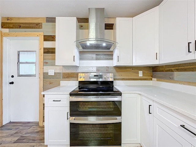 kitchen featuring wall chimney exhaust hood, tasteful backsplash, stainless steel range with electric cooktop, light hardwood / wood-style floors, and white cabinets