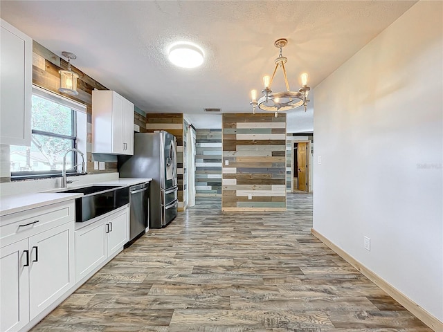 kitchen with stainless steel appliances, sink, decorative light fixtures, a notable chandelier, and white cabinetry