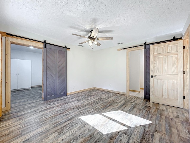 unfurnished bedroom featuring a barn door, ceiling fan, and wood-type flooring