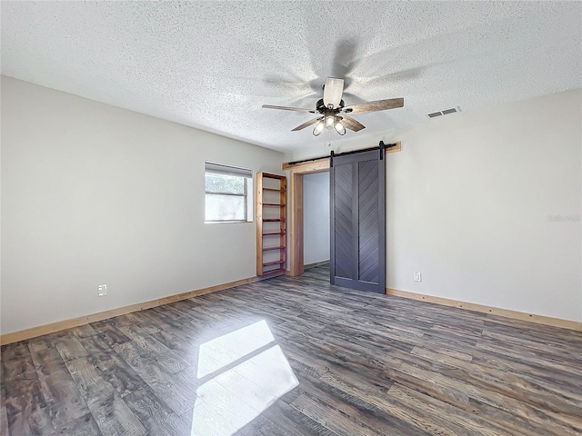 unfurnished bedroom with ceiling fan, a barn door, dark hardwood / wood-style flooring, and a textured ceiling