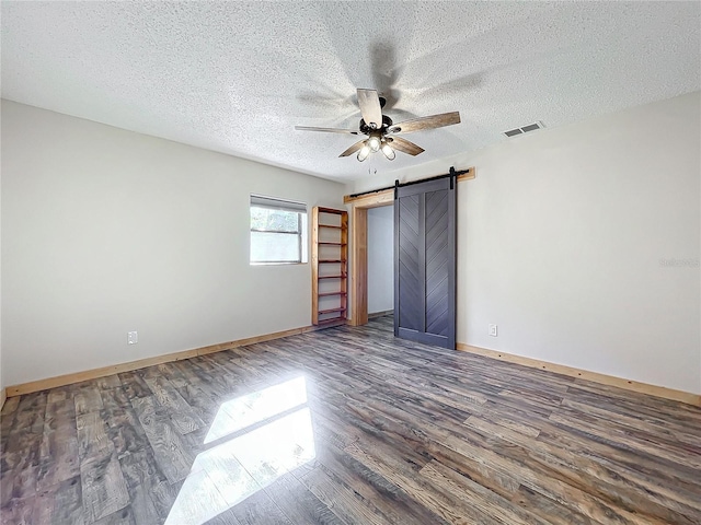 unfurnished bedroom with a barn door, ceiling fan, dark hardwood / wood-style flooring, and a textured ceiling