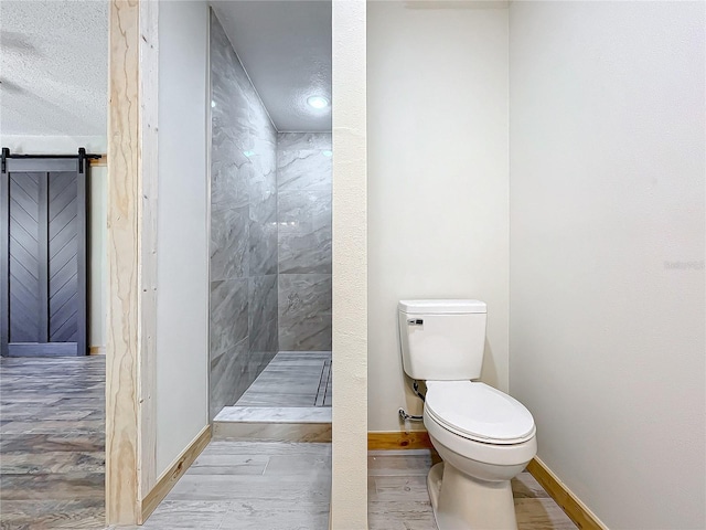 bathroom with toilet, wood-type flooring, a textured ceiling, and a tile shower