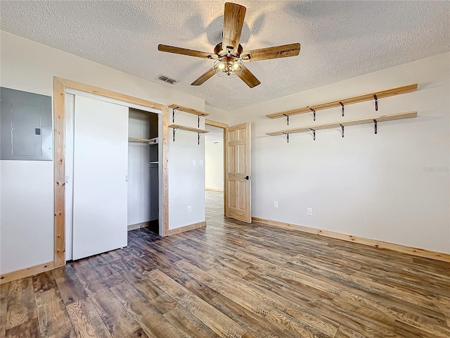 unfurnished bedroom featuring electric panel, ceiling fan, a textured ceiling, dark hardwood / wood-style flooring, and a closet