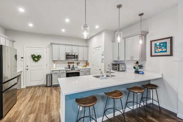 kitchen featuring kitchen peninsula, sink, hanging light fixtures, a kitchen breakfast bar, and stainless steel appliances