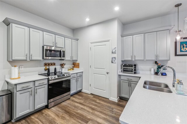 kitchen featuring dark hardwood / wood-style floors, gray cabinets, sink, hanging light fixtures, and appliances with stainless steel finishes