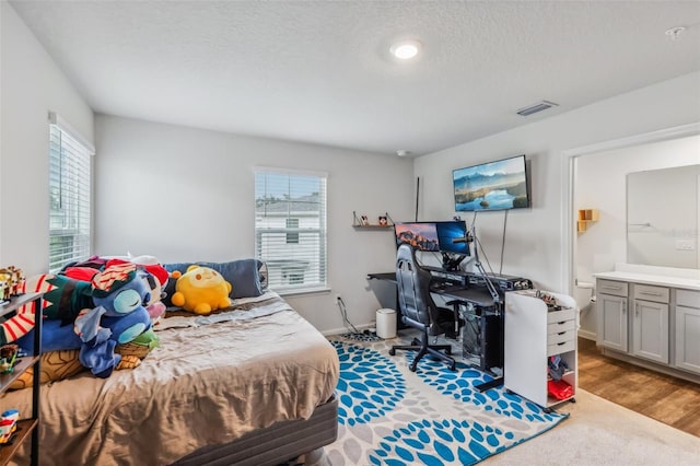 bedroom featuring a textured ceiling, light hardwood / wood-style floors, multiple windows, and ensuite bath