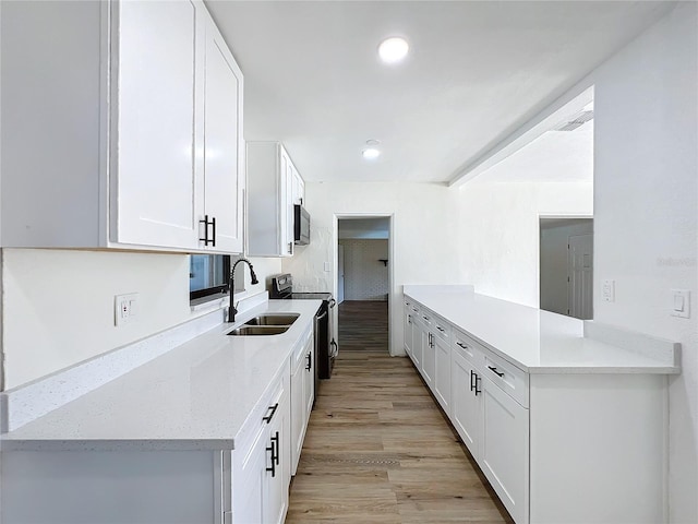 kitchen with light stone counters, stainless steel appliances, sink, light hardwood / wood-style floors, and white cabinetry