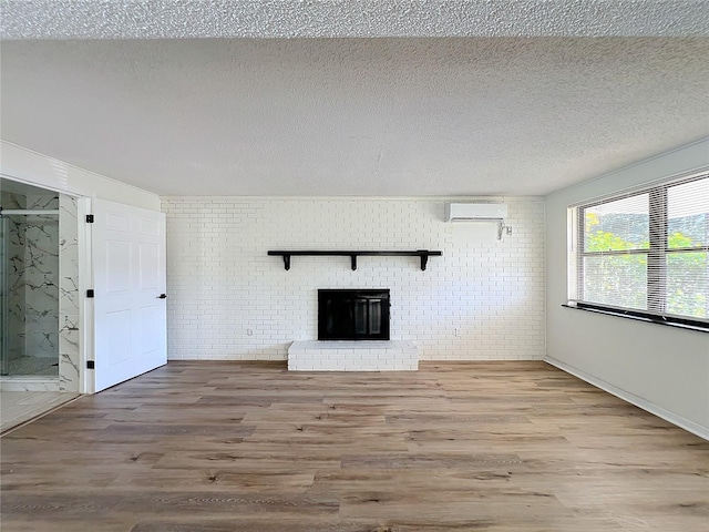 unfurnished living room with a wall mounted air conditioner, a brick fireplace, hardwood / wood-style flooring, a textured ceiling, and brick wall