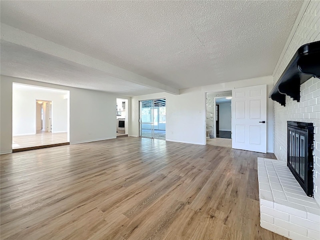 unfurnished living room featuring a brick fireplace, a textured ceiling, and light hardwood / wood-style flooring