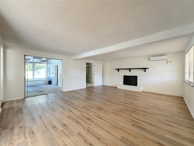 unfurnished living room with a brick fireplace, brick wall, a textured ceiling, a wall mounted AC, and light hardwood / wood-style floors