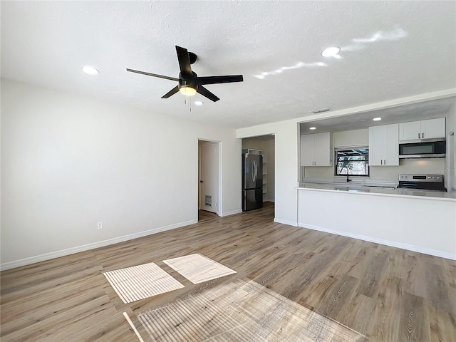 unfurnished living room featuring ceiling fan, a textured ceiling, and light wood-type flooring