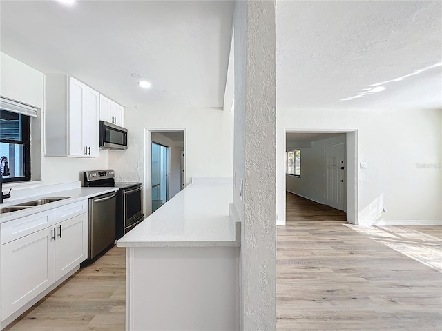 kitchen with sink, light stone countertops, light wood-type flooring, appliances with stainless steel finishes, and white cabinetry