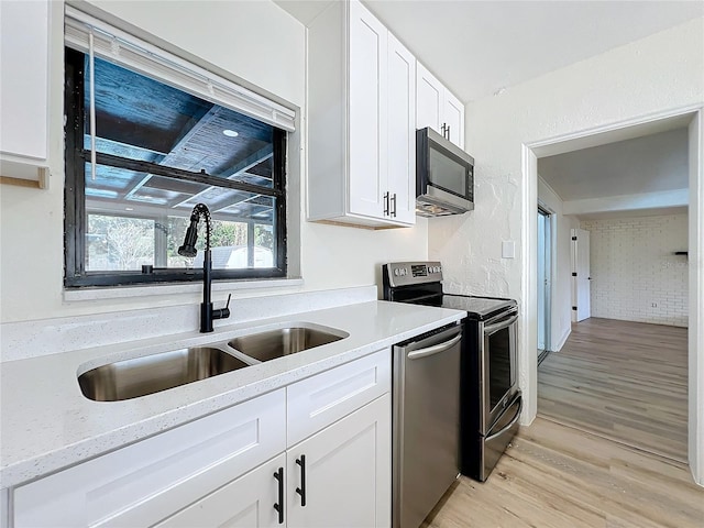 kitchen with light stone countertops, appliances with stainless steel finishes, sink, white cabinets, and light hardwood / wood-style floors