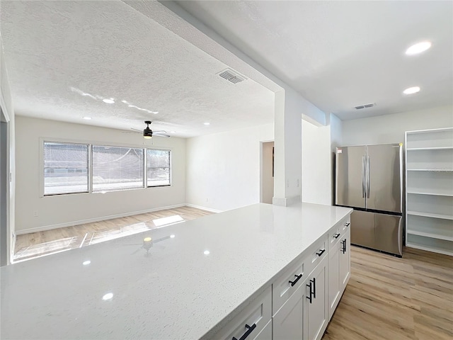 kitchen featuring light stone counters, ceiling fan, white cabinetry, light hardwood / wood-style floors, and stainless steel refrigerator