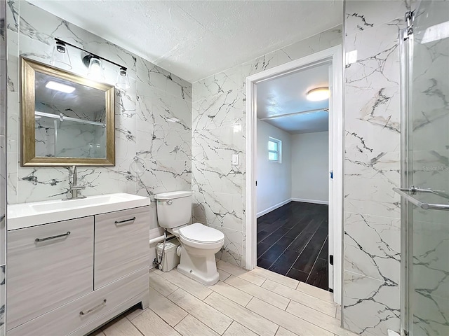 bathroom featuring a textured ceiling, toilet, a shower with door, vanity, and tile walls