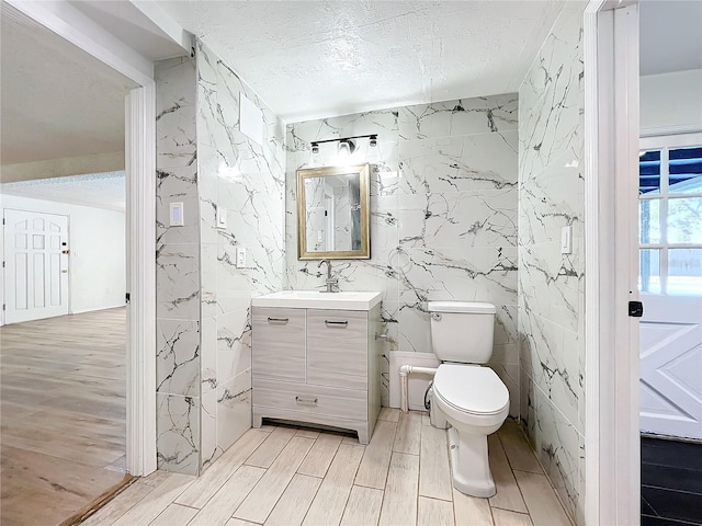 bathroom with vanity, toilet, a textured ceiling, tile walls, and wood-type flooring