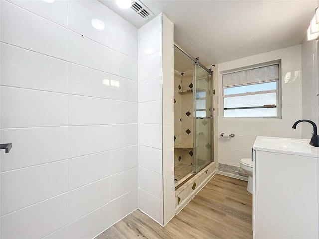 bathroom with walk in shower, vanity, hardwood / wood-style flooring, tile walls, and toilet