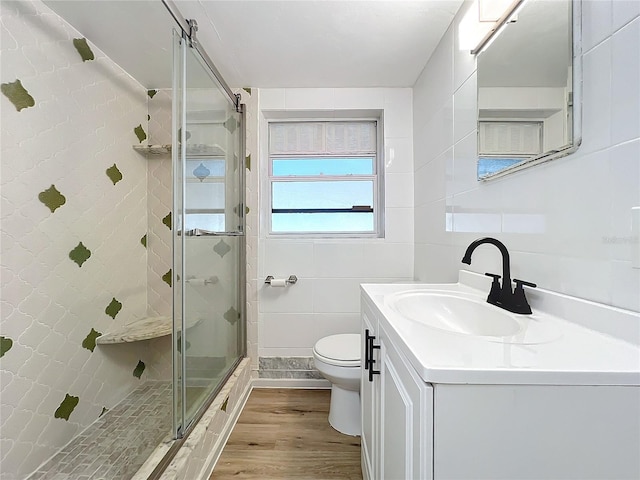 bathroom with wood-type flooring, toilet, a shower with door, vanity, and tile walls