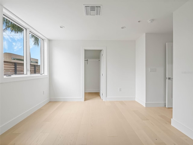 unfurnished bedroom featuring a walk in closet and light hardwood / wood-style flooring