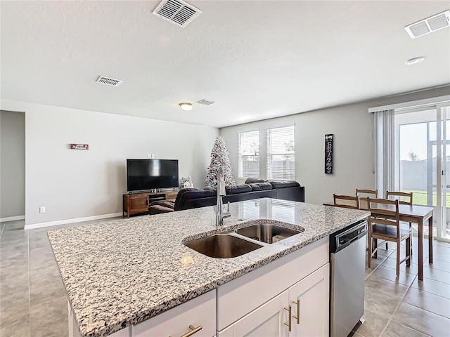 kitchen with light stone countertops, stainless steel dishwasher, sink, white cabinetry, and an island with sink