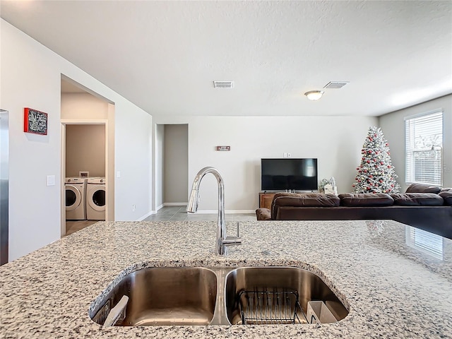 kitchen with washing machine and dryer, light stone countertops, and sink