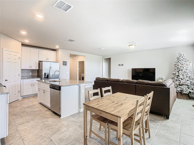 kitchen with a kitchen island with sink, white cabinets, sink, light stone counters, and stainless steel appliances