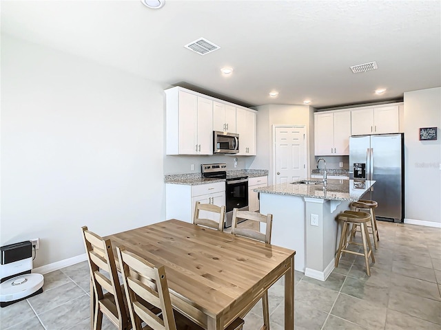 kitchen with sink, stainless steel appliances, light stone counters, a kitchen island with sink, and white cabinets